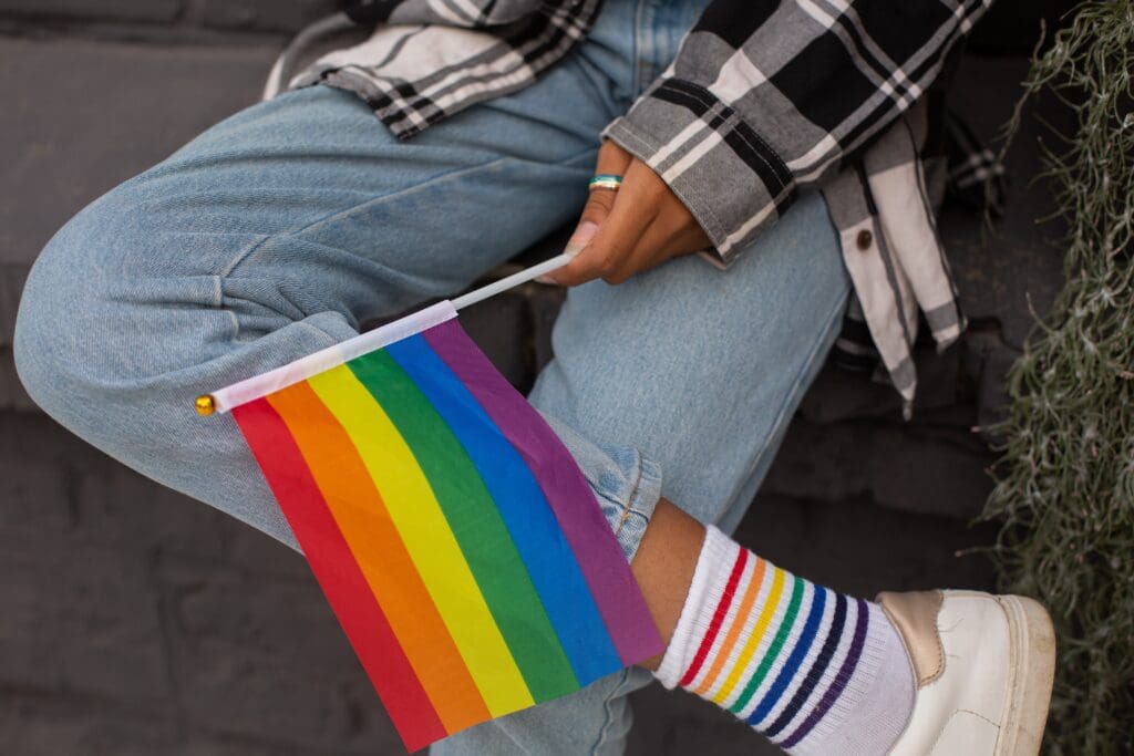 A person sitting on the ground holding a rainbow flag.