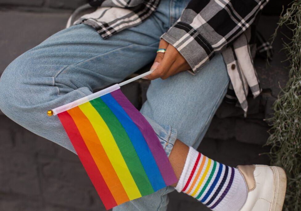 A person sitting on the ground holding a rainbow flag.